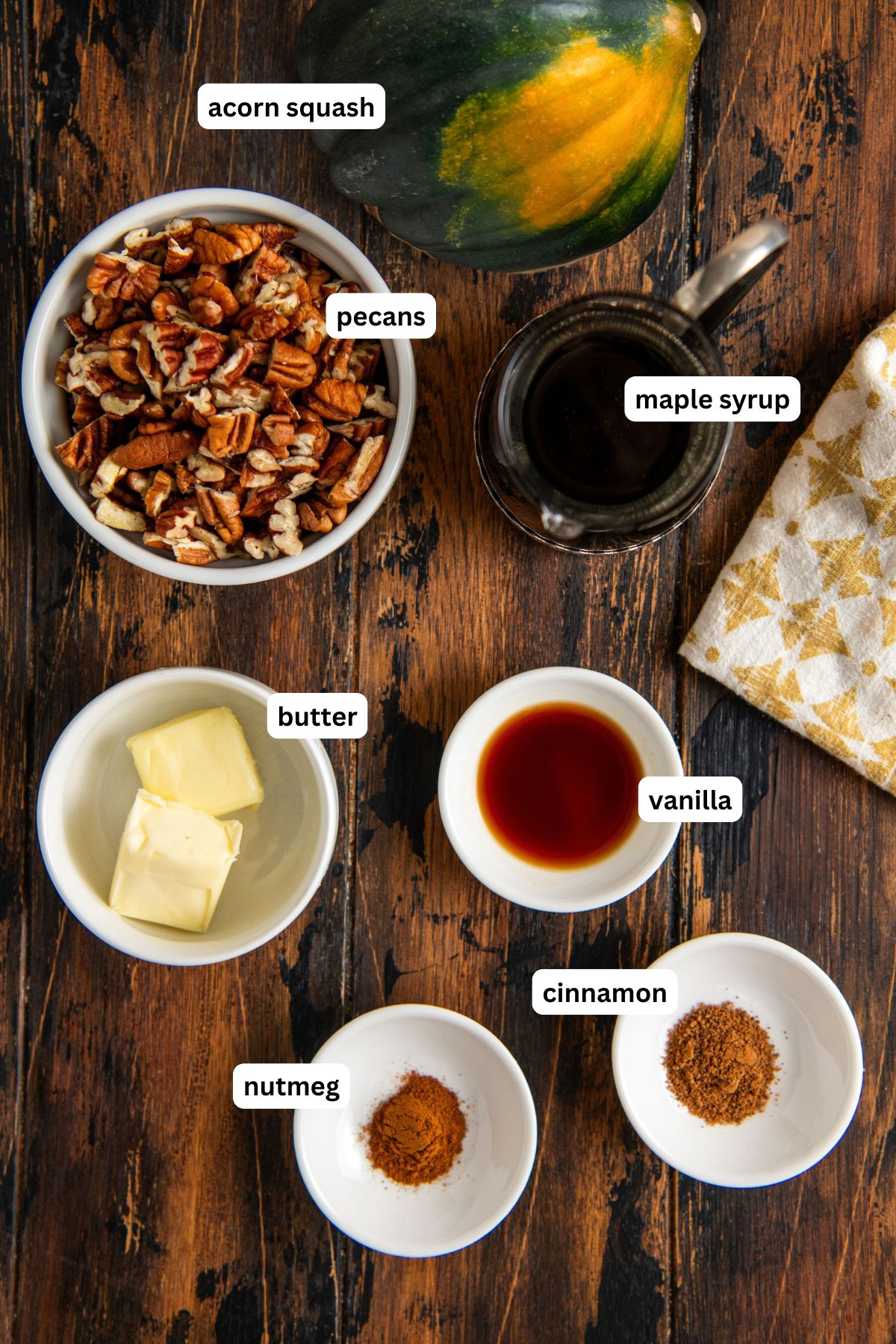 Labeled ingredients for maple pecan baked acorn squash: acorn squash, chopped pecans, maple syrup, butter, vanilla extract, ground nutmeg, and ground cinnamon.