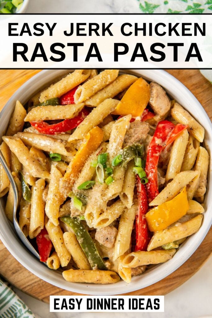 A bowl of chicken rasta pasta with jerk chicken, red, yellow, and green bell peppers, garnished with sliced green onions and grated cheese.