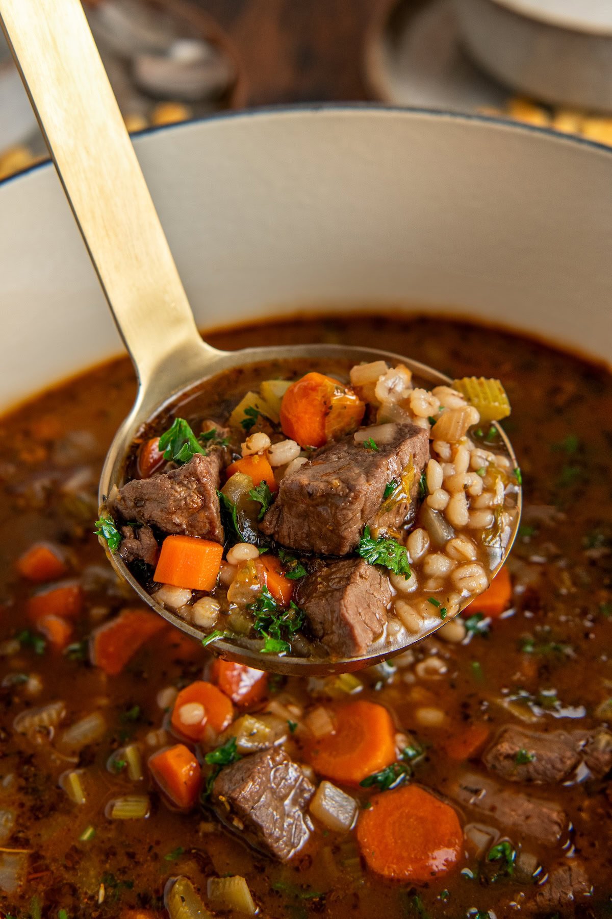 Made easy in one-pot, Beef Barley Soup is loaded with tender beef, chewy pearl barley, and lots of vegetables in a rich and savory broth. A ladle lifts a hearty beef and barley vegetable soup with chunks of beef, carrots, celery, barley, and fresh herbs from a pot. The broth is rich and brown, with visible seasonings and colorful vegetables.