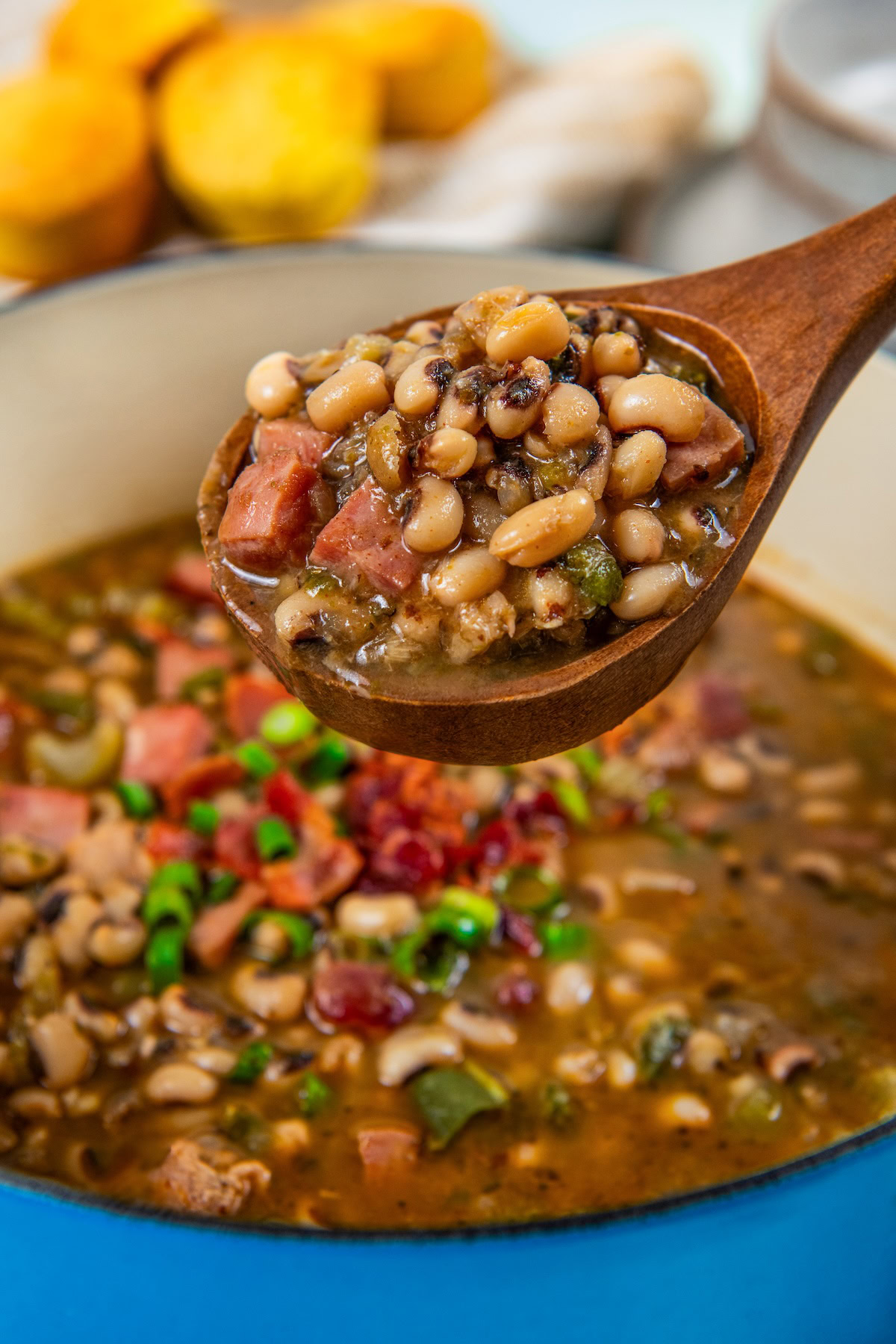 Slowly simmered in a rich and smoky broth, these Southern Black Eyed Peas are insanely flavorful and tender as can be! A wooden spoon holds a serving of black eyed peas with ham and chopped vegetables above a full pot.