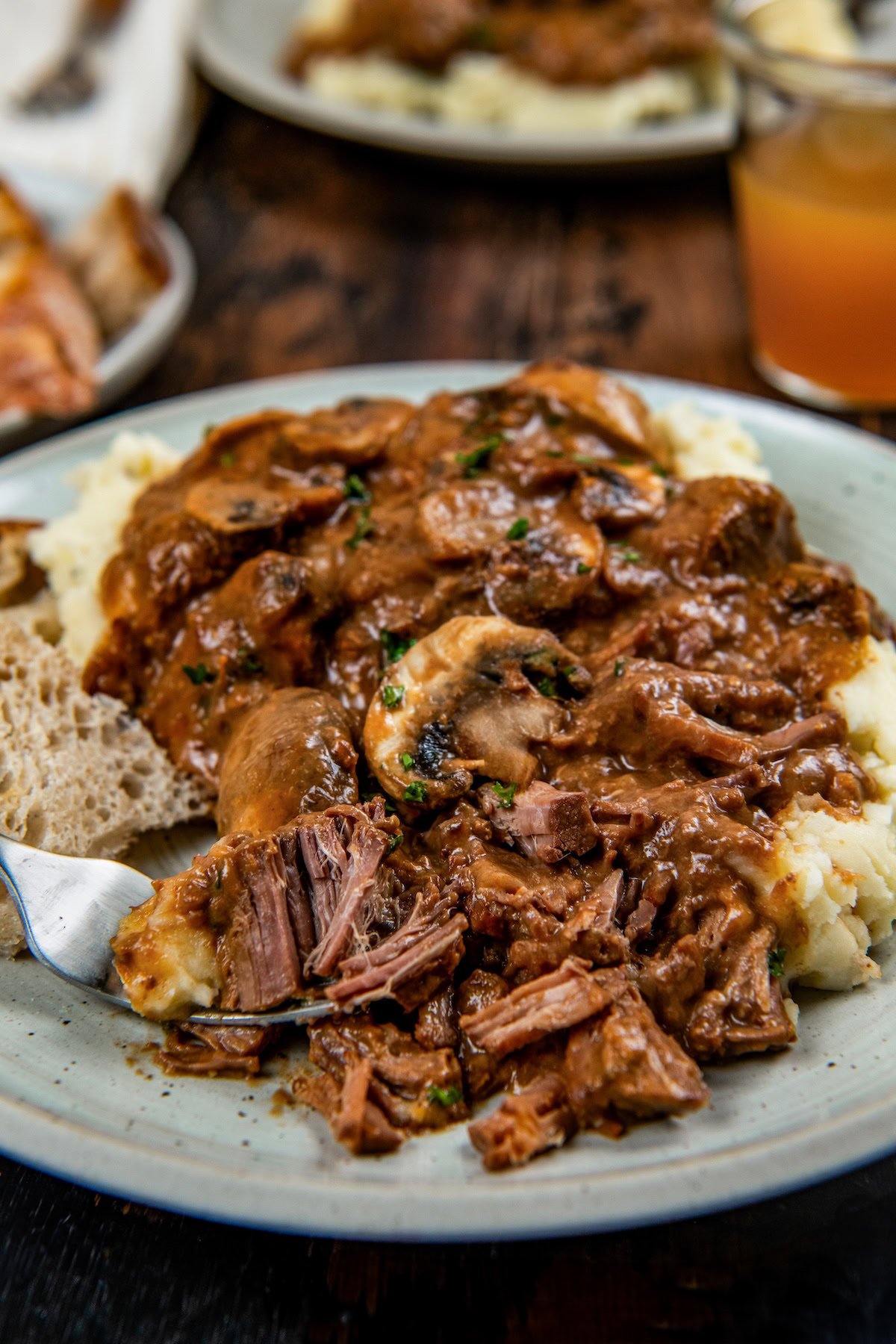 This easy Crockpot Steak Diane recipe slowly simmers ultra-tender beef and hearty mushrooms in a rich, creamy, and savory sauce. A plate of mashed potatoes topped with tender slow cooker steak Diane with rich brown gravy and mushrooms with fresh herbs on top.