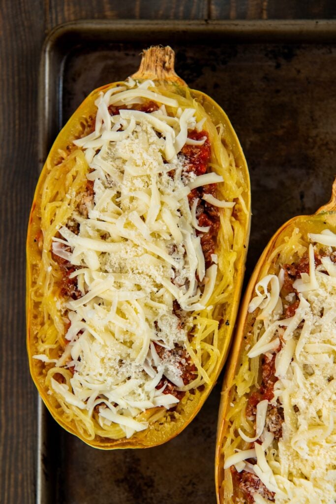 Stuffed spaghetti squash filled with a saucy ground meat mixture and gooey melted cheese. A hearty, low-carb comfort food with a veggie twist. A halved roasted spaghetti squash filled with a meat and marinara sauce, topped with shredded mozzarella and grated Parmesan cheese, sits on a dark baking sheet.