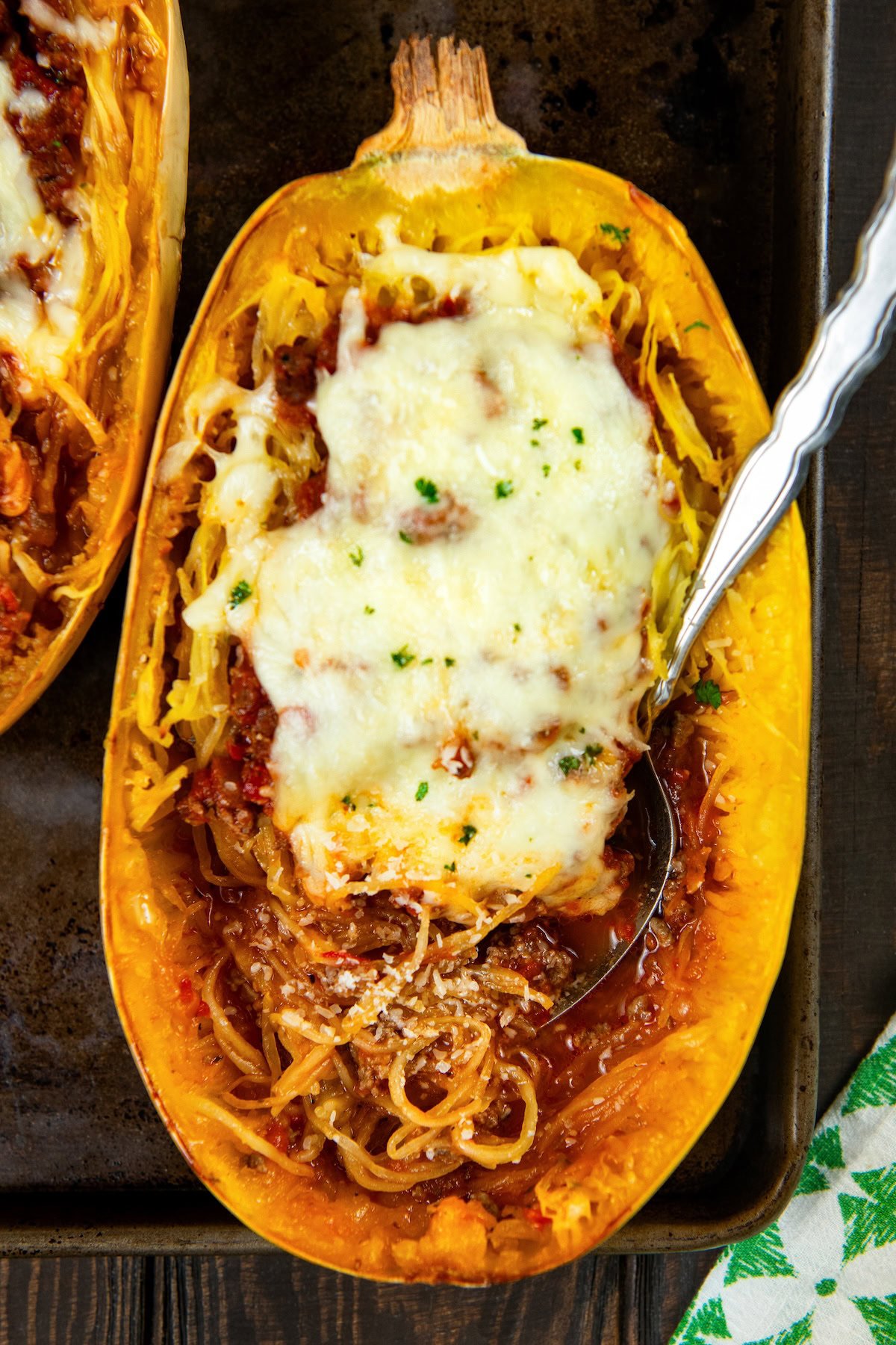 Stuffed spaghetti squash filled with a saucy ground meat mixture and gooey melted cheese. A hearty, low-carb comfort food with a veggie twist. A baked stuffed spaghetti squash half filled with tomato sauce, ground meat, and topped with melted cheese and herbs sits on a baking sheet with a spoon inside.