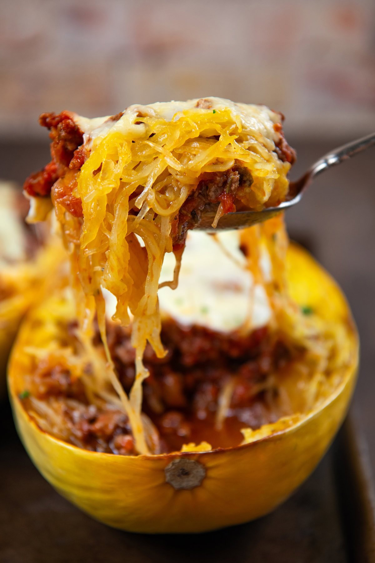 Stuffed spaghetti squash filled with a saucy ground meat mixture and gooey melted cheese. A hearty, low-carb comfort food with a veggie twist. A fork lifts a serving of stuffed spaghetti squash with a rich tomato meat sauce and melted cheese from a halved squash.