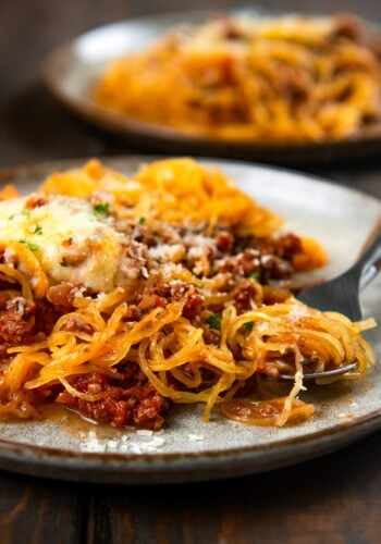 A plate of spaghetti squash topped with meat sauce, melted cheese, and herbs, with a fork twirling some of the squash.