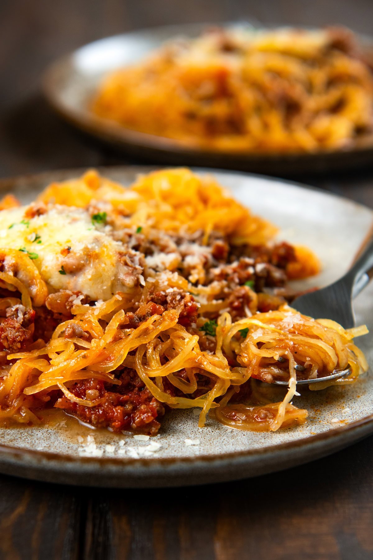 Stuffed spaghetti squash filled with a saucy ground meat mixture and gooey melted cheese. A hearty, low-carb comfort food with a veggie twist. A plate of spaghetti squash topped with meat sauce, melted cheese, and herbs, with a fork twirling some of the squash.