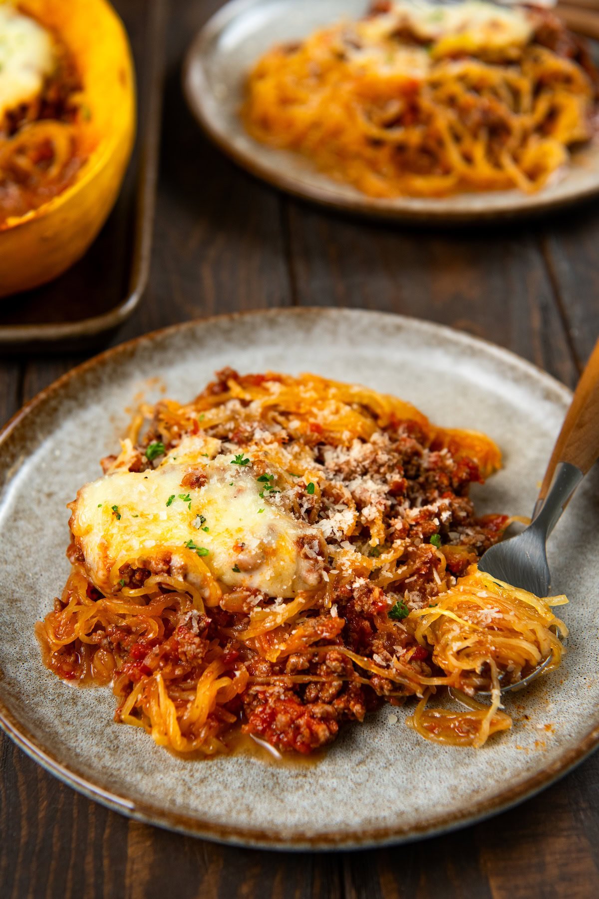 Stuffed spaghetti squash filled with a saucy ground meat mixture and gooey melted cheese. A hearty, low-carb comfort food with a veggie twist. Two plates of stuffed spaghetti squash with meat sauce and melted cheese.