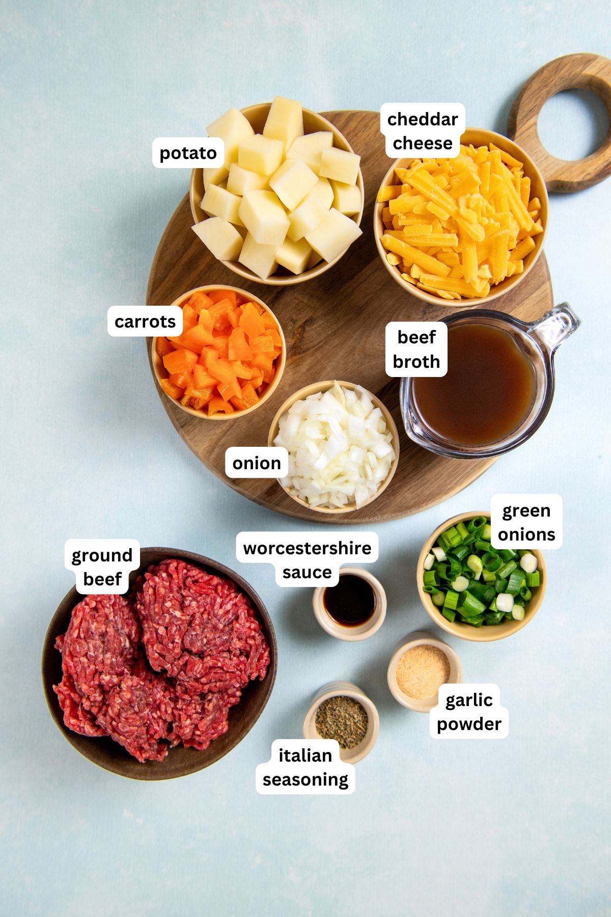 Ground beef, potatoes, and plenty of cheese combine to make this Hamburger Hash recipe, an easy one-pot dinner that's ready in 30 minutes! A top-down view of bowls containing ingredients for a hamburger hash recipe: diced potato, shredded cheddar cheese, chopped carrots, beef broth, chopped onion, sliced green onions, ground beef, Worcestershire sauce, Italian seasoning, and garlic powder.