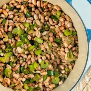 Learn how to cook pinto beans to tender and creamy perfection in a smoky, flavorful broth with bacon, jalapeño, onion, and more. A blue pot filled with soaked pinto beans mixed with chopped jalapeños and onions, sitting on a light surface next to a striped kitchen towel.