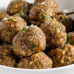 A white bowl filled with several golden-brown baked turkey meatballs garnished with grated parmesan cheese and chopped herbs.