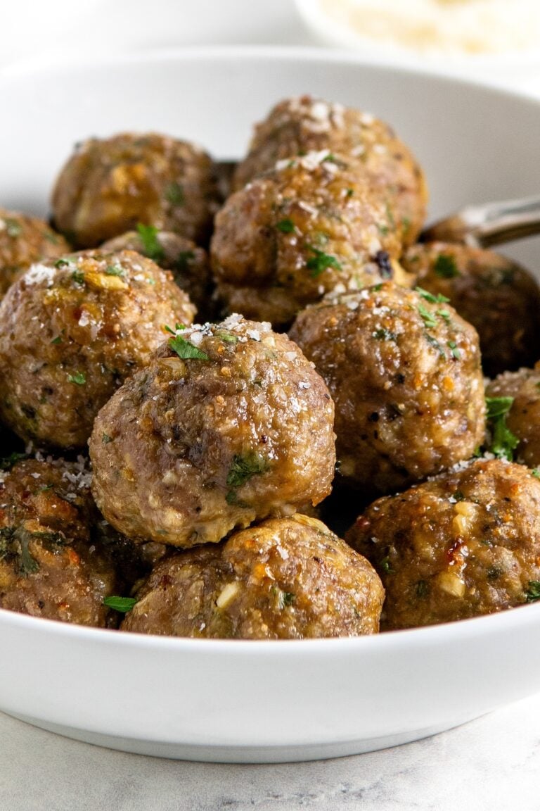 A white bowl filled with several golden-brown baked turkey meatballs garnished with grated parmesan cheese and chopped herbs.