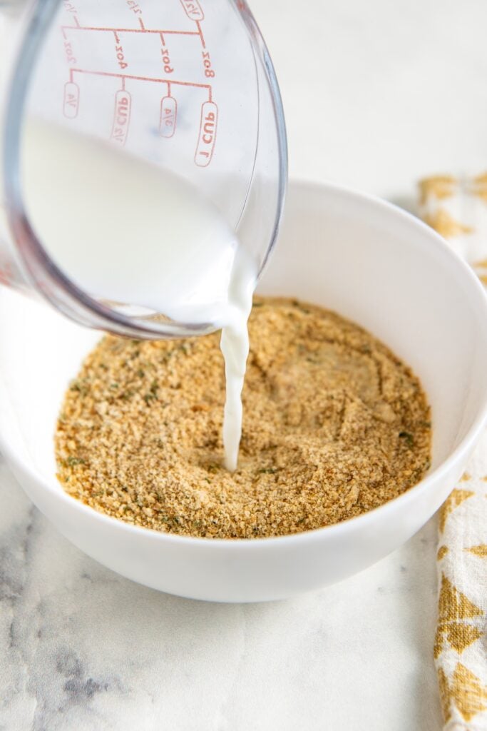 This easy Turkey Meatball recipe uses a few simple tricks and the perfect ingredient ratios to make moist, delicious meatballs every time! A measuring cup pours milk into a white bowl filled with seasoned breadcrumbs.