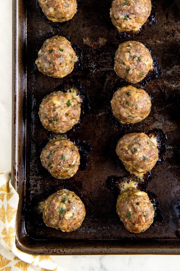 This easy Turkey Meatball recipe uses a few simple tricks and the perfect ingredient ratios to make moist, delicious meatballs every time! A baking sheet holds rows of browned, baked turkey meatballs with melted cheese oozing from some.