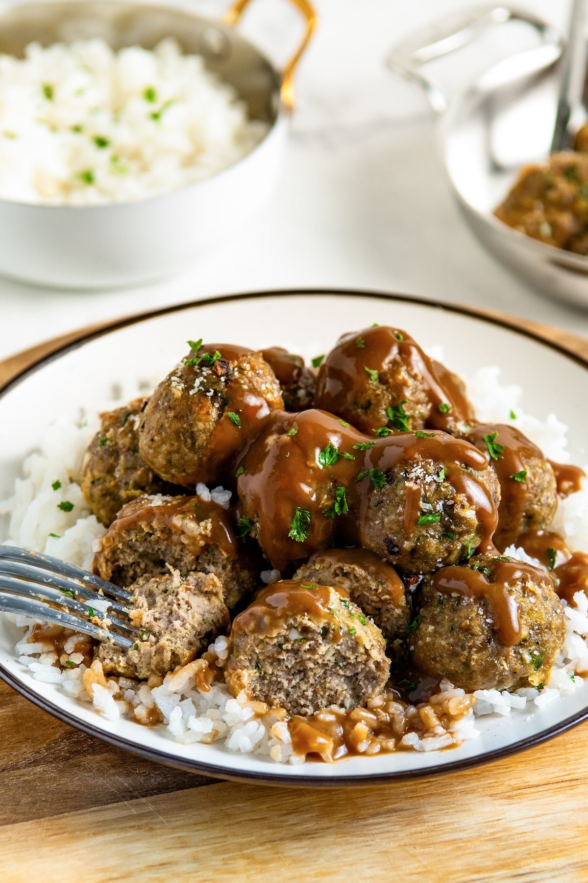 This easy Turkey Meatball recipe uses a few simple tricks and the perfect ingredient ratios to make moist, delicious meatballs every time! A plate of white rice topped with turkey meatballs covered in brown gravy and garnished with chopped herbs. A fork is cutting into one meatball to show the inside.