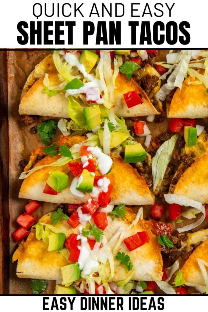 A sheet pan filled with baked tacos topped with lettuce, diced tomatoes, avocado, cilantro, and drizzled with sour cream.