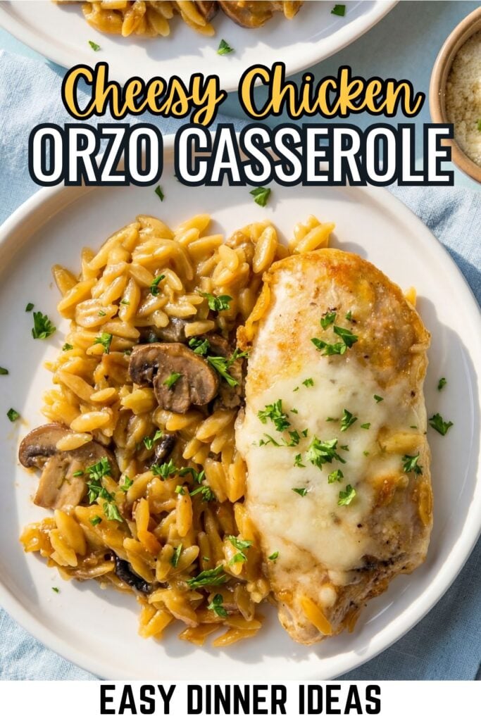 Plate with cheesy baked chicken breast and creamy orzo casserole with mushrooms, garnished with chopped herbs.
