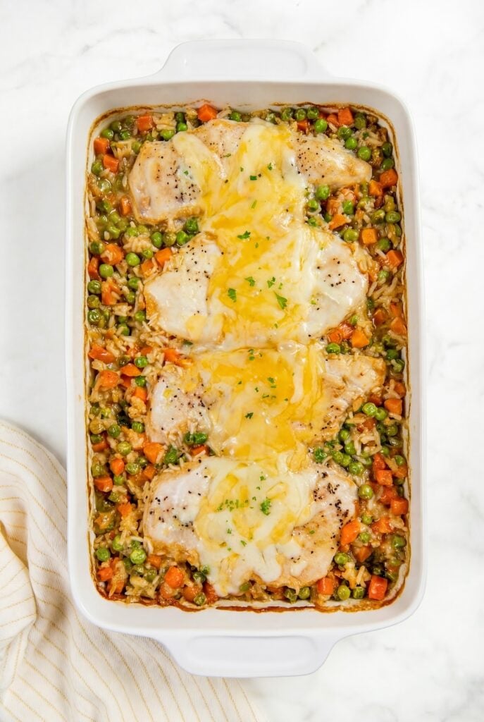 This easy chicken and rice casserole recipe is pure creamy, cheesy comfort food every single time. One pan, 5 minutes of prep, and dinner is done! A cheesy chicken and rice casserole with peas and carrots in a white 9x13 casserole dish.