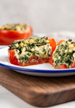 A close-up of a stuffed tomato filled with a creamy spinach and cheese mixture, the tomato is cut in half to show the filling.