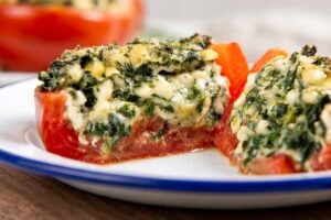 A close-up of a stuffed tomato filled with a creamy spinach and cheese mixture, the tomato is cut in half to show the filling.
