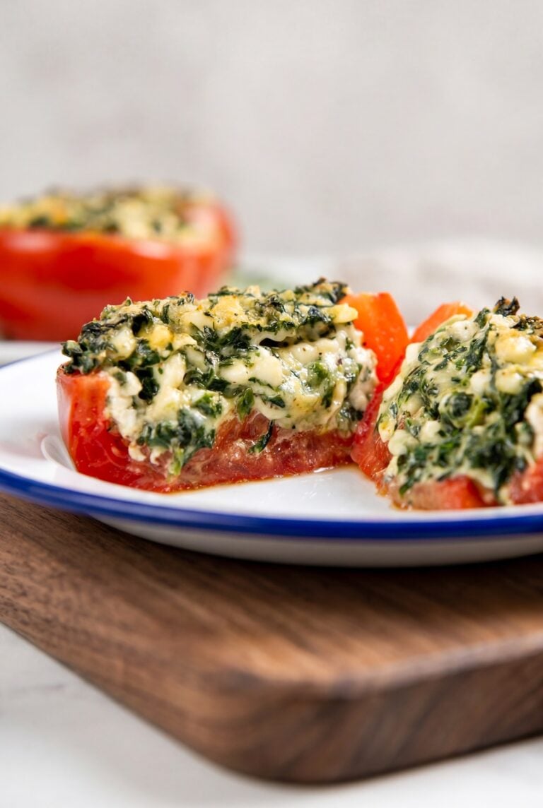 A close-up of a stuffed tomato filled with a creamy spinach and cheese mixture, the tomato is cut in half to show the filling.