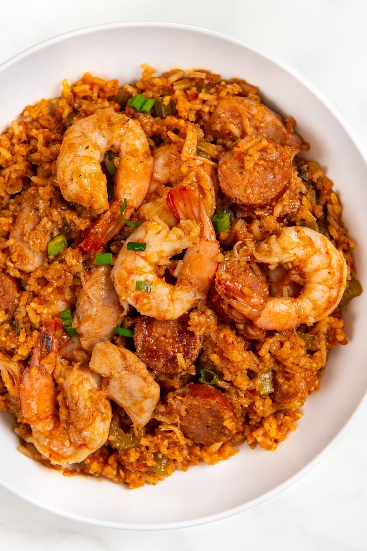 Full of bold Cajun flavor, this easy jambalaya recipe is a one-pot Louisiana classic loaded with chicken, andouille sausage, and shrimp. A white bowl filled with cajun jambalaya, featuring shrimp, sausage slices, diced vegetables, and seasoned rice in a reddish sauce, garnished with chopped green onions.