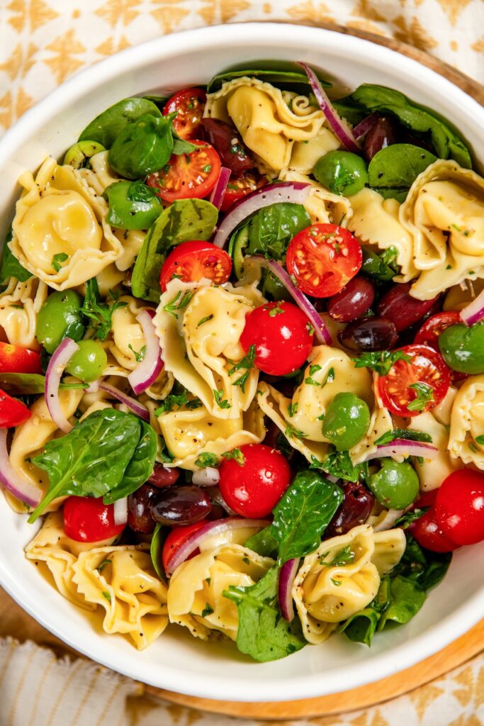 Cheese Tortellini Pasta Salad recipe with cherry tomatoes, spinach, olives, and a fresh lemon dressing is a summer favorite ready in just 15 minutes! A bowl of cheese tortellini pasta salad with cherry tomatoes, spinach, olives, red onion slices, and fresh herbs, tossed in a light vinaigrette.