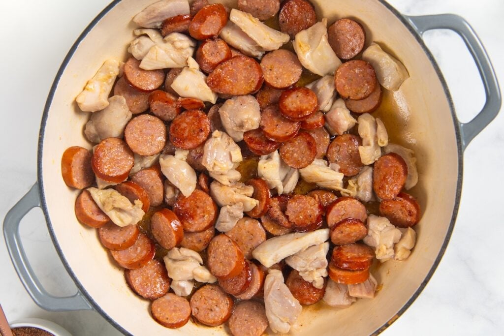 Full of bold Cajun flavor, this easy jambalaya recipe is a one-pot Louisiana classic loaded with chicken, andouille sausage, and shrimp. A pot filled with sliced sausage and chunks of chicken being cooked, with both meats browned and sizzling in oil.