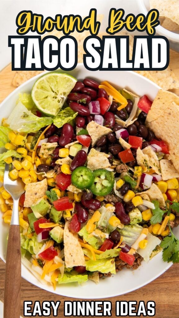 A bowl of ground beef taco salad topped with lettuce, corn, black beans, kidney beans, tomatoes, shredded cheese, jalapeños, tortilla chips, and lime slices. Text reads: Ground Beef Taco Salad - Easy Dinner Ideas.