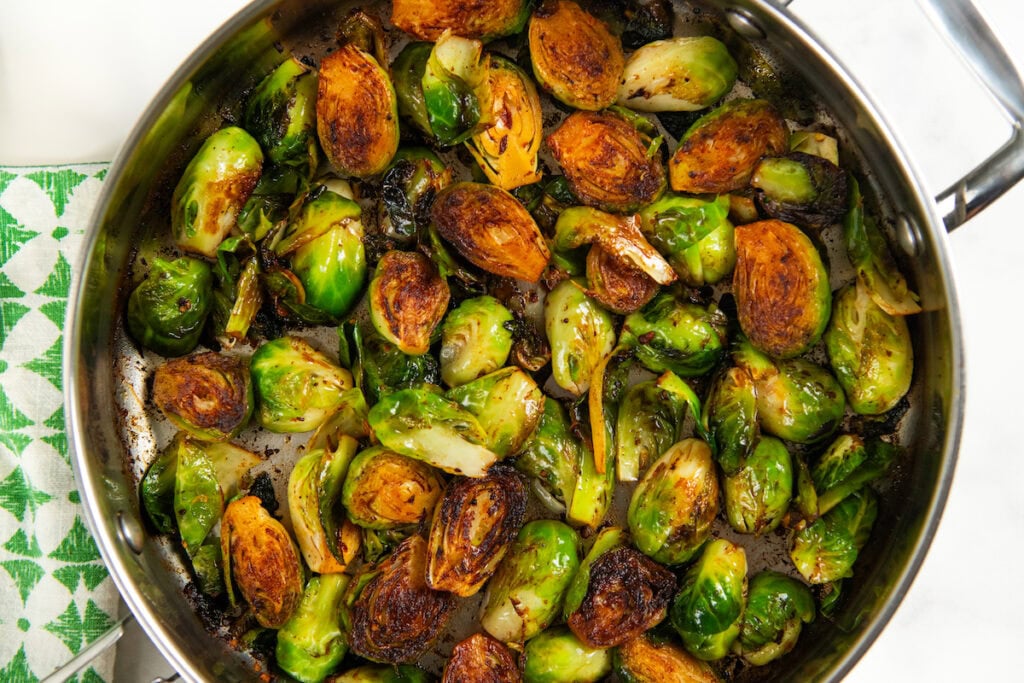 Hot Honey Brussels Sprouts with crispy bacon, caramelized sprouts, and a sweet-spicy honey drizzle. One skillet, ready in 25 minutes! A skillet filled with halved Brussels sprouts that are pan-seared and caramelized, showing browned, crispy edges and green centers.