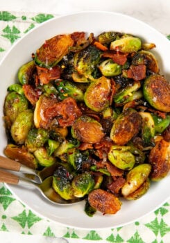 A white bowl filled with hot honey Brussels sprouts mixed with crispy bacon pieces and topped with chili flakes and flaky sea salt.