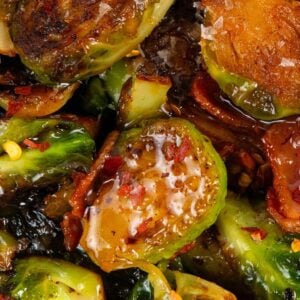 Close-up of hot honey Brussels sprouts mixed with crispy bacon and coated in a shiny hot honey glaze, garnished with red pepper flakes.