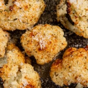 Close-up of roasted Parmesan Ranch Roasted Cauliflower topped with grated cheese and spices, resting on a dark baking tray. The florets appear golden brown and crispy.