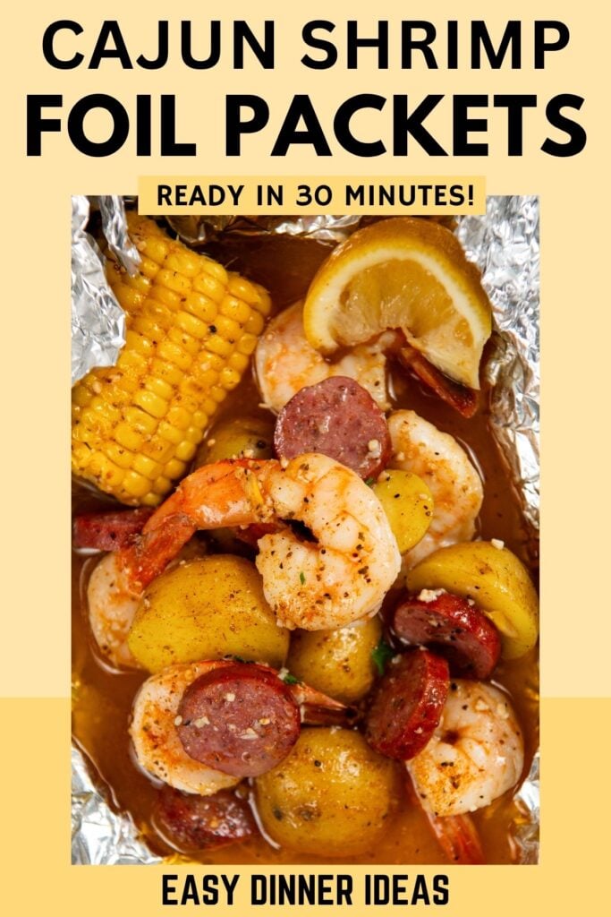 A shrimp foil packet filled with Cajun shrimp, sausage slices, corn on the cob, potato chunks, and lemon wedges.