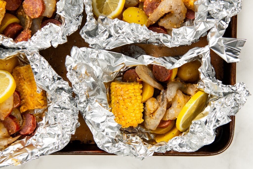 Shrimp Foil Packets bring all the flavor of a shrimp boil with garlic butter, sausage, corn, and potatoes. Ready in about 30 minutes! Shrimp boil foil packets filled with sliced sausage, shrimp, yellow potatoes, corn on the cob, and lemon wedges sit on a baking sheet, ready to be cooked.