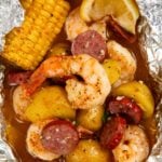 Shrimp foil packet filled with cooked shrimp, sliced sausage, small potatoes, corn on the cob, and a lemon wedge, all seasoned and covered in a flavorful broth.