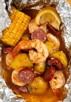 Shrimp foil packet filled with cooked shrimp, sliced sausage, small potatoes, corn on the cob, and a lemon wedge, all seasoned and covered in a flavorful broth.