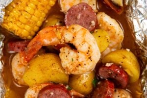 Shrimp foil packet filled with cooked shrimp, sliced sausage, small potatoes, corn on the cob, and a lemon wedge, all seasoned and covered in a flavorful broth.