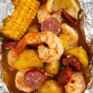 Shrimp foil packet filled with cooked shrimp, sliced sausage, small potatoes, corn on the cob, and a lemon wedge, all seasoned and covered in a flavorful broth.