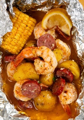 Shrimp foil packet filled with cooked shrimp, sliced sausage, small potatoes, corn on the cob, and a lemon wedge, all seasoned and covered in a flavorful broth.