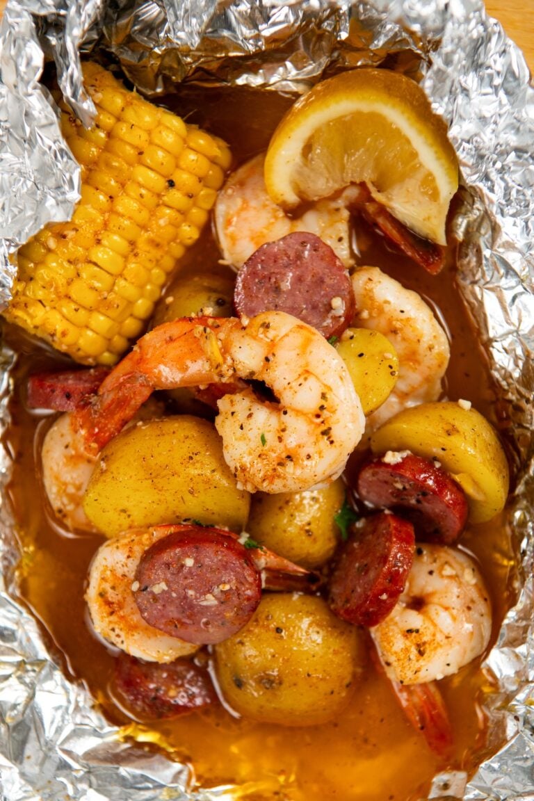 Shrimp foil packet filled with cooked shrimp, sliced sausage, small potatoes, corn on the cob, and a lemon wedge, all seasoned and covered in a flavorful broth.