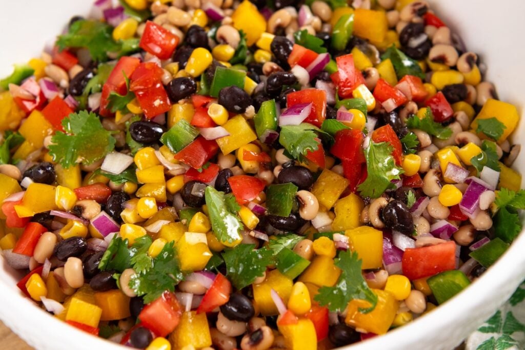 Best made in advance, Cowboy Caviar dip is fresh, colorful, and full of black beans, corn, and crunchy veggies in a tangy lime dressing. Colorful cowboy caviar with black beans, black-eyed peas, corn, red onion, red and yellow bell peppers, cilantro, and green jalapeño pieces coated in dressing in a large white bowl.