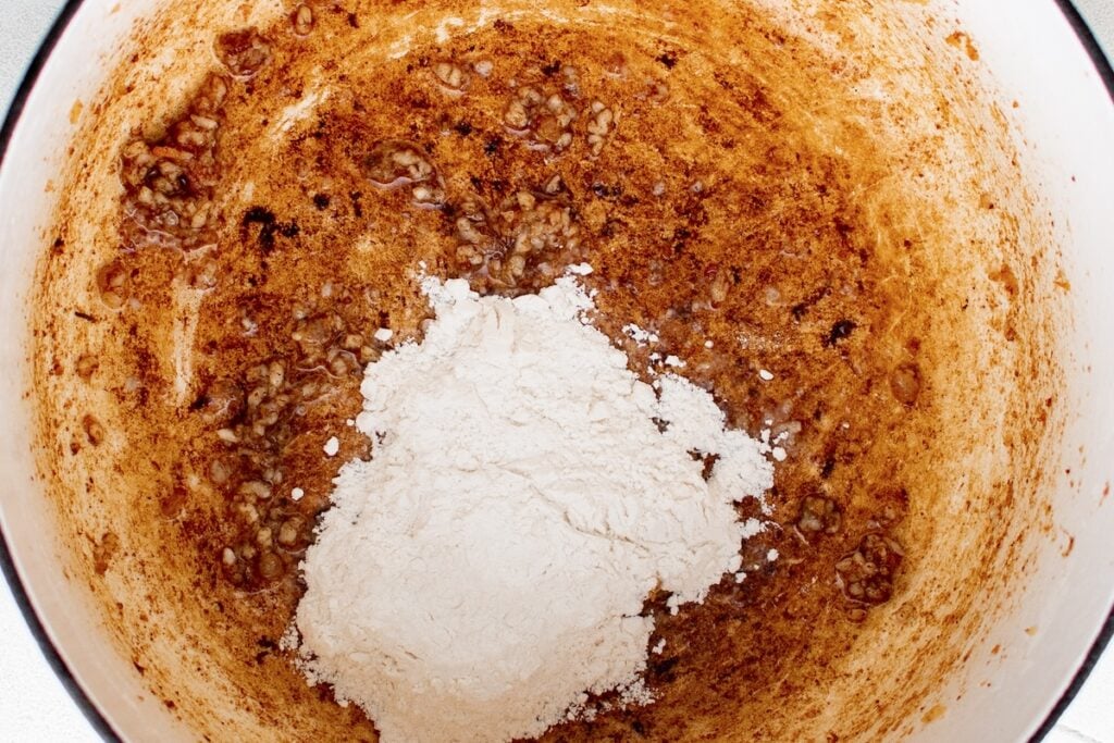 A white pot with browned bits and a scoop of flour on the bottom to be mixed into a roux.