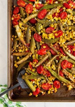 Sheet pan with oven roasted okra and tomatoes with corn. A metal spatula is partially visible on the bottom left.