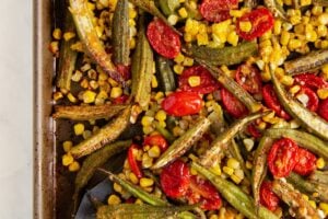Sheet pan with oven roasted okra and tomatoes with corn. A metal spatula is partially visible on the bottom left.