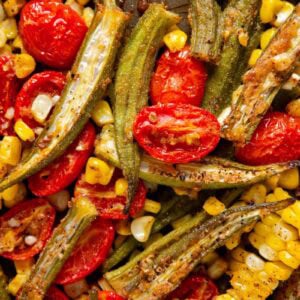 Close-up of roasted okra and tomatoes with corn that has been seasoned with spices. The vegetables are slightly charred, vibrant, and arranged together, showing texture and color variety in a cooked vegetable medley.
