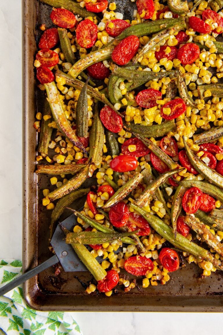 Sheet pan with oven roasted okra and tomatoes with corn. A metal spatula is partially visible on the bottom left.