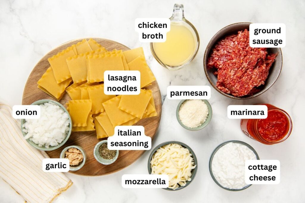 Skillet Lasagna is a quick one pan spin on the classic. No boiling, no layering, and a golden broiled cheese top in about 30 minutes! Lasagna ingredients for skillet lasagna recipe arranged on a marble board: uncooked noodles, ground sausage, chicken broth, diced onion, parmesan, marinara sauce, garlic, Italian seasoning, mozzarella, and cottage cheese. Each item is labeled.