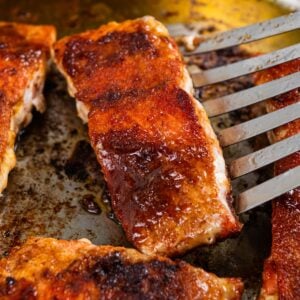 Brown sugar salmon fillets cooking in a pan, with a spatula lifting one piece.
