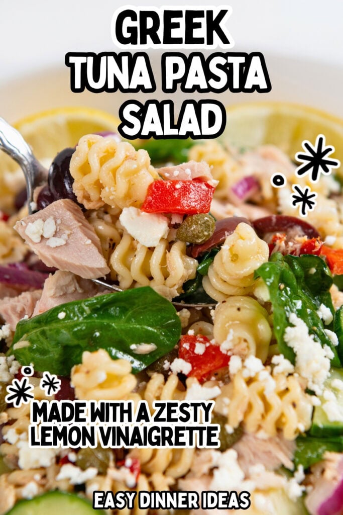 Close-up of Greek tuna pasta salad with rotini, spinach, olives, tomatoes, feta, and lemon slices, topped with text: Greek Tuna Pasta Salad, Made with a Zesty Lemon Vinaigrette, Easy Dinner Ideas.