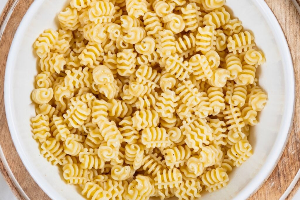 Greek Tuna Pasta Salad has salty olives, cool cucumber, and creamy feta in a lemon garlic dressing. No mayo, no oven, ready in 30 minutes! A white bowl filled with cooked pasta noodles.